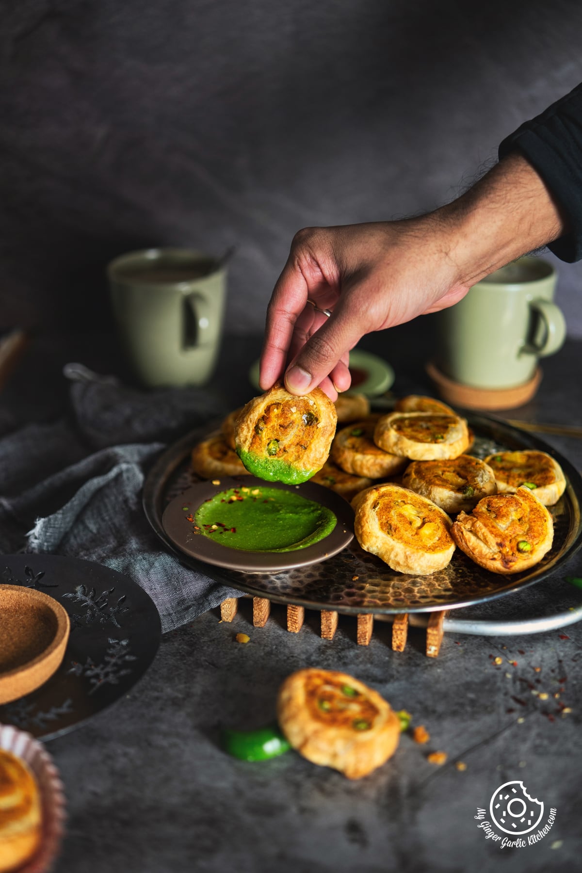 a person holding a samosa pinwheel over a plate of green chutney with more samosa pinwheels on the side