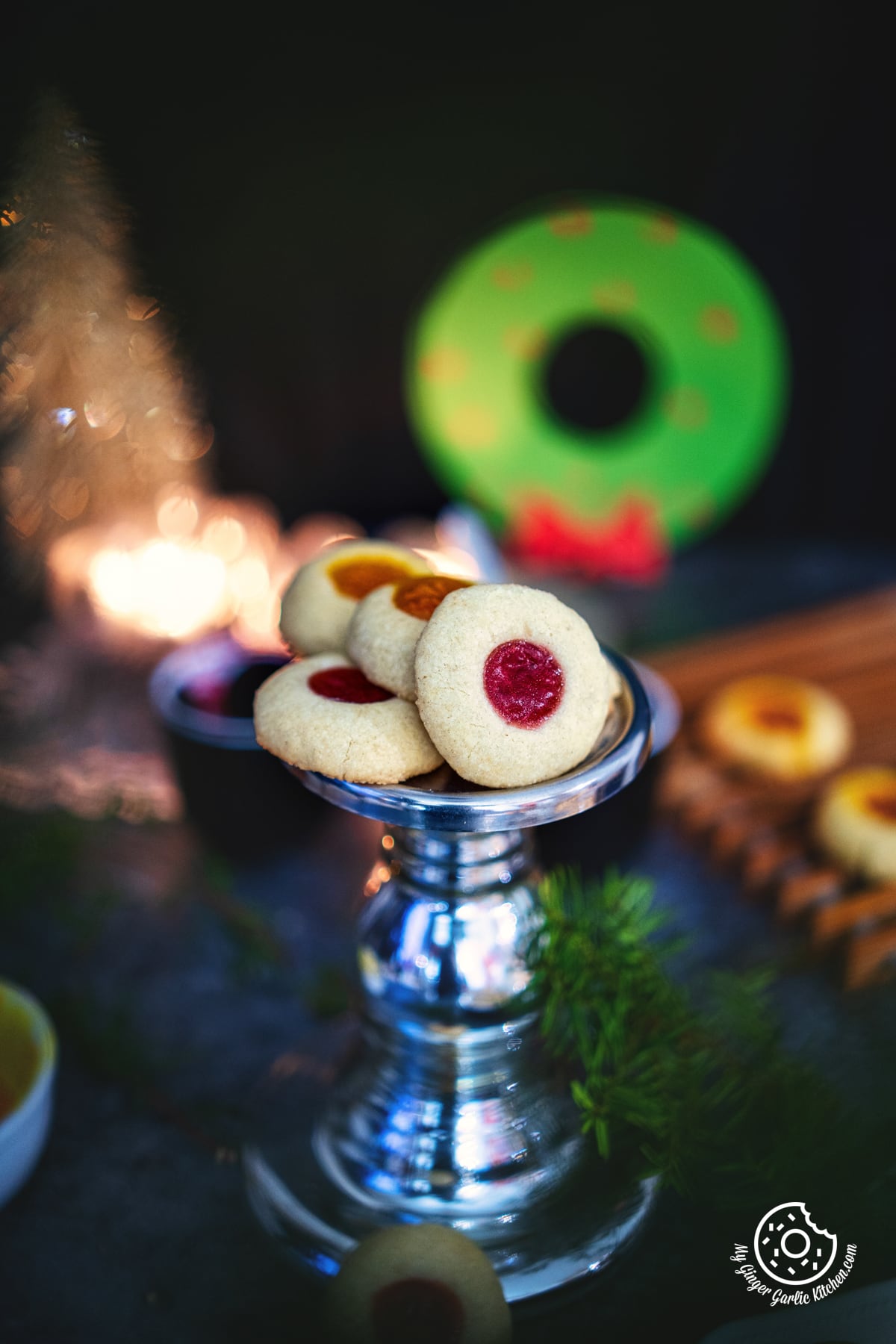 four eggless thumbprint cookies stacked on metal stand with a candle in background