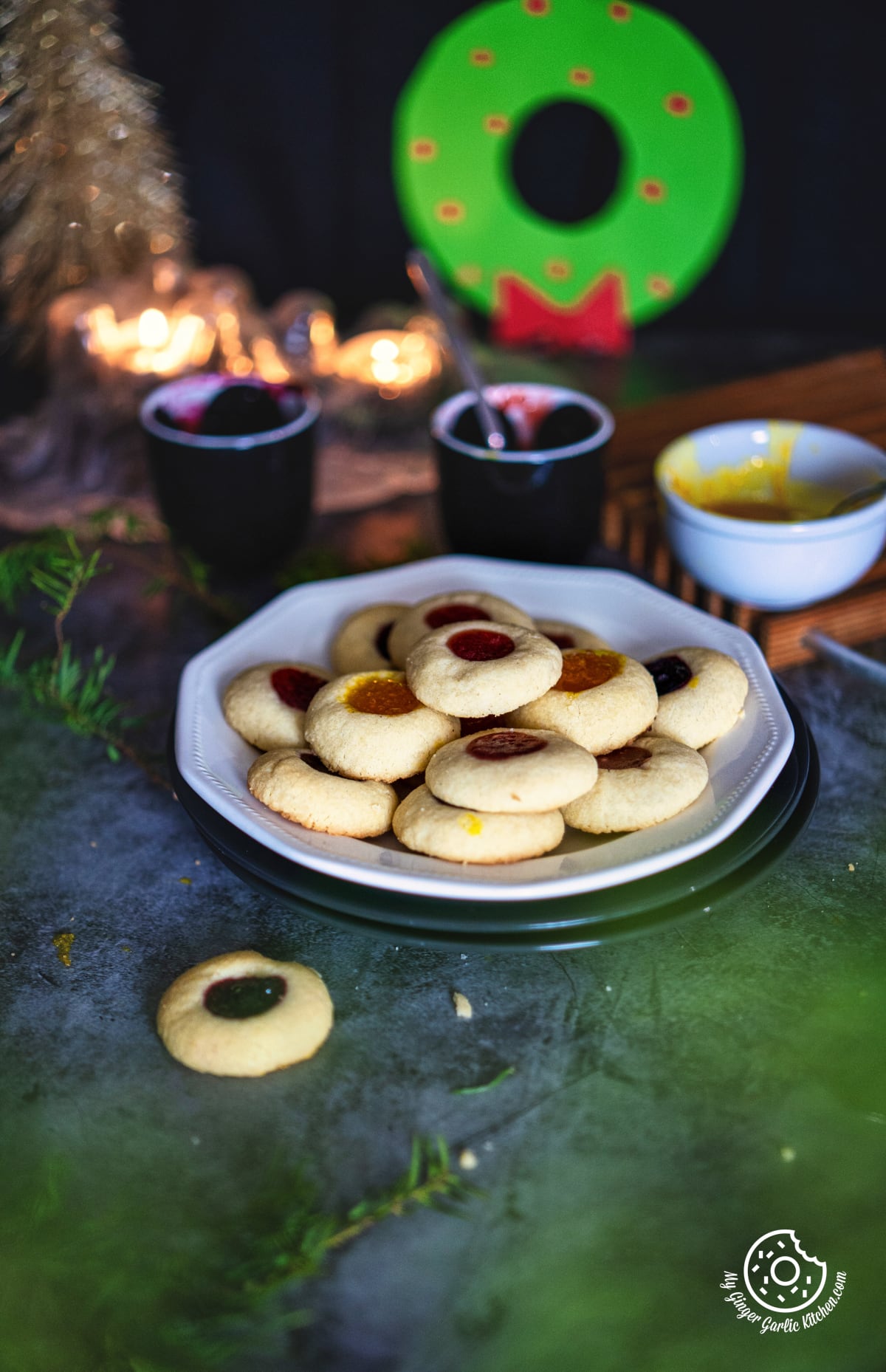 a batch of thumbprint cookies filled with jam arranged on a white late with a cookie with jam bowls in the background