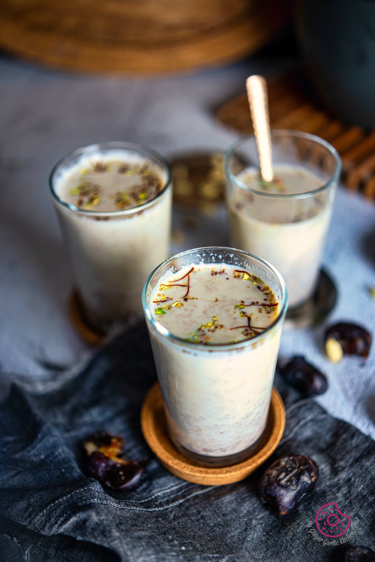 close up of date milk in 3 transparent glasses with some dates and cardamom on the side