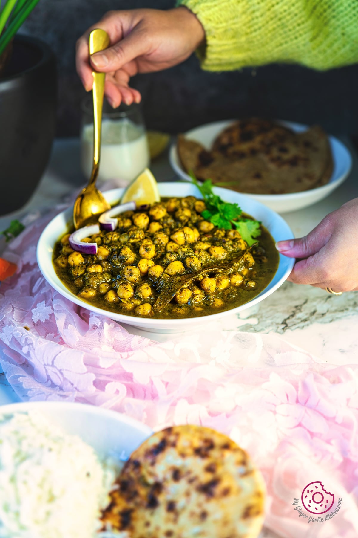 a hand holding a golden spoon over a white bowl palak chole