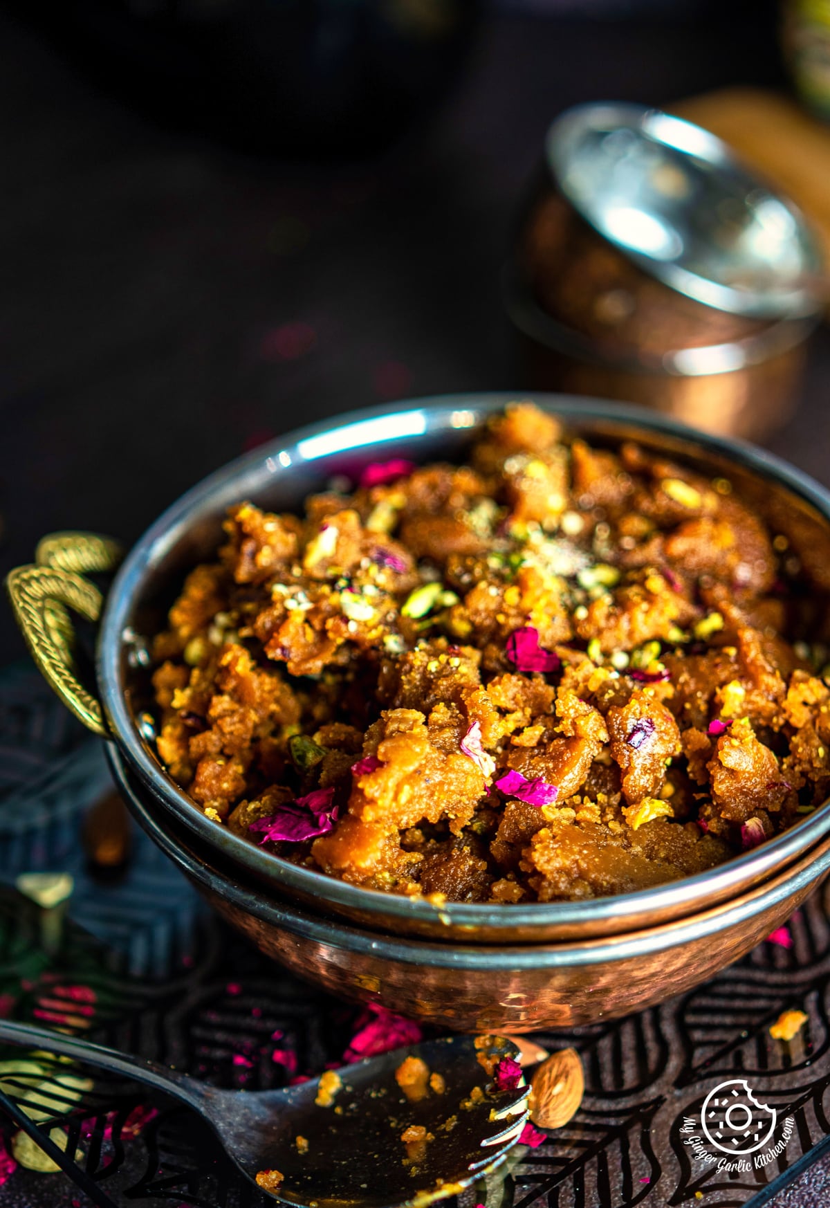 a close up of a besan halwa garnished with dry fruits kept in a copper kadai