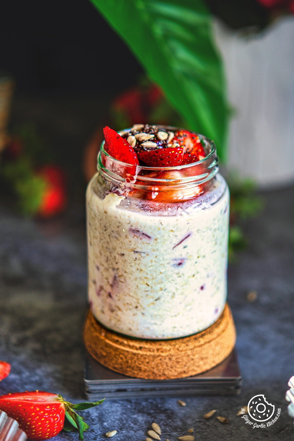 closeup strawberry overnight oats in a glass jar topped with strawberries, sun flower seeds, and chia seeds