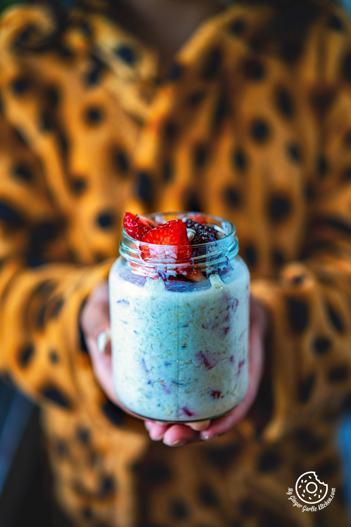 closeup of a kid holding a strawberry overnight oats topped with strawberries in a glass jar