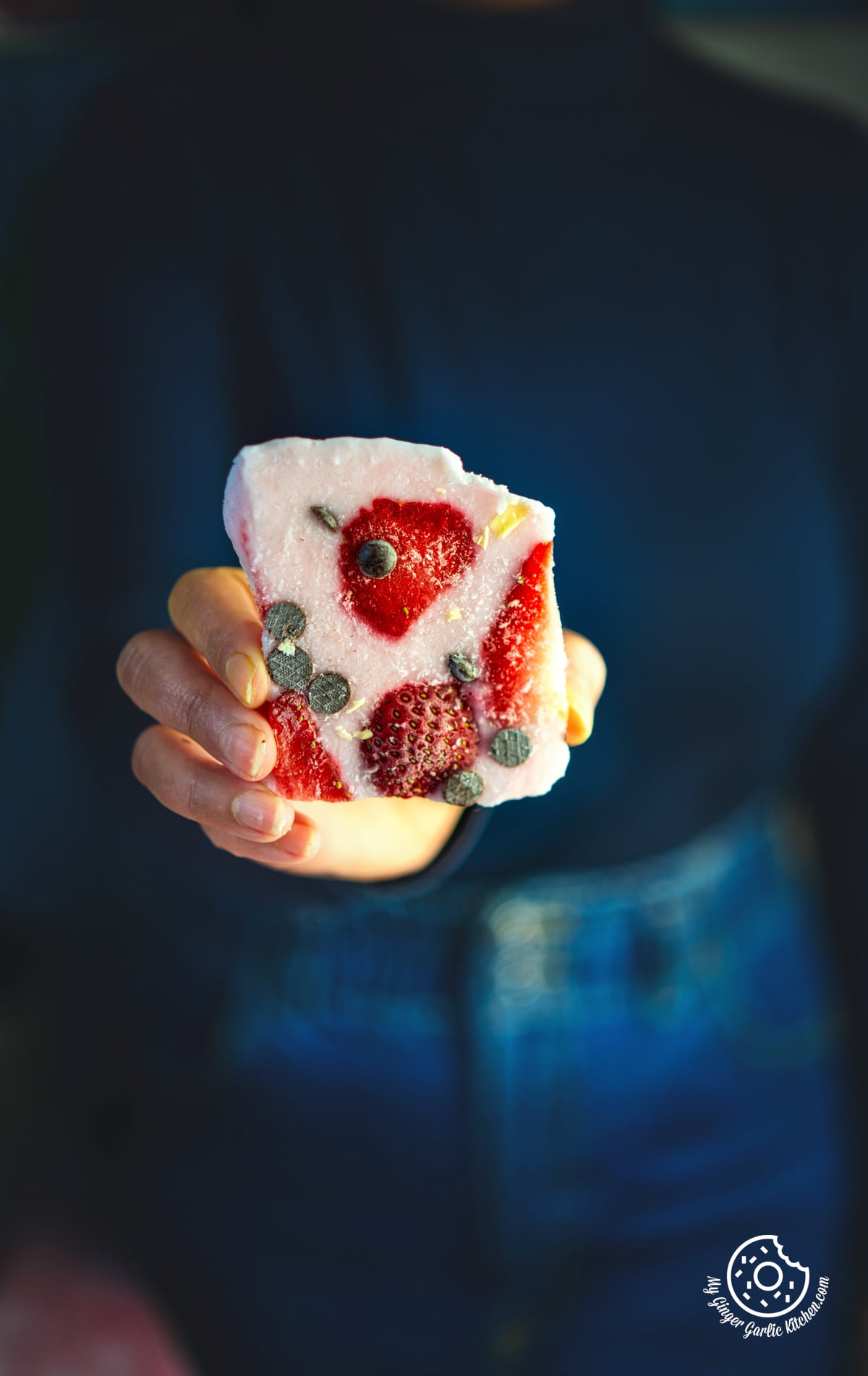 a close up of a person holding a piece of strawberry yogurt  bark topped with chocolate chips and strawberries