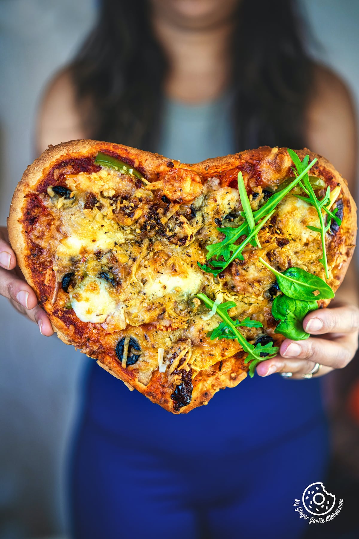 a close up of a female holding a vegetarian heart pizza