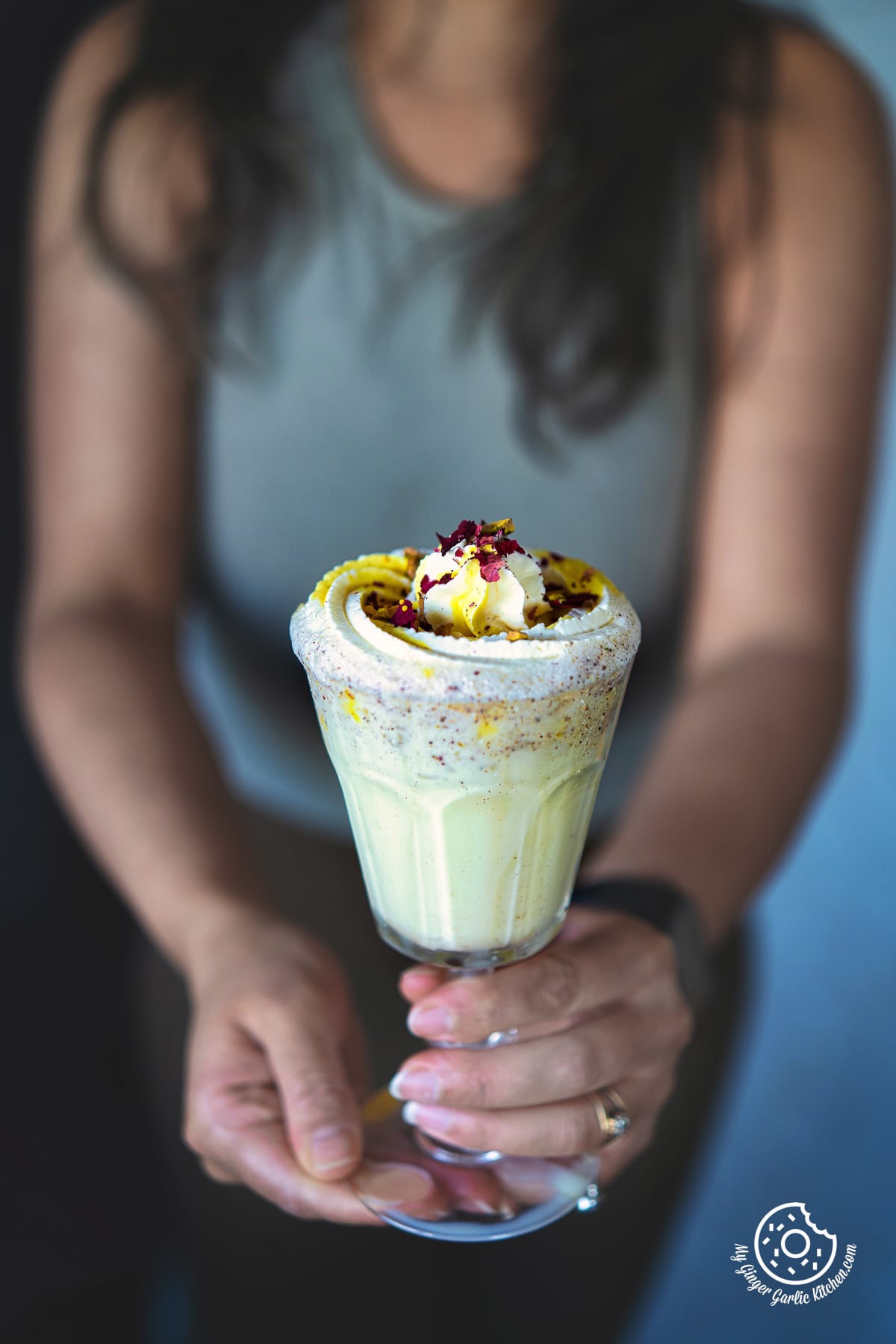 a female holding a thandai frappe glass with whipped cream and rose petals