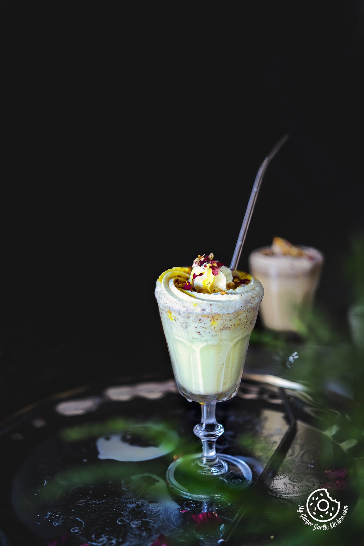 a glass of thandai frappe topped with whipped cream and rose petals
