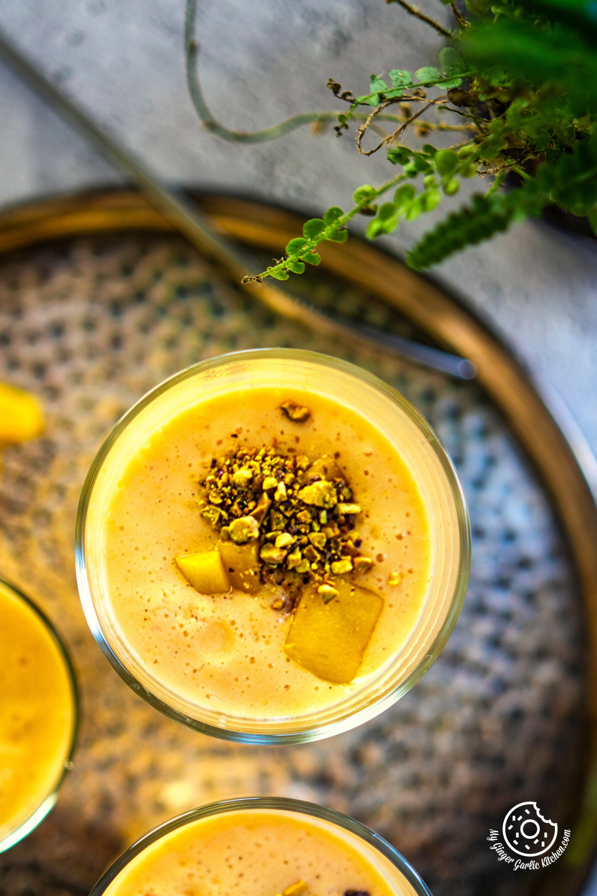 close up overhead mango lassi glass topped with chopped mangoes and pistachio