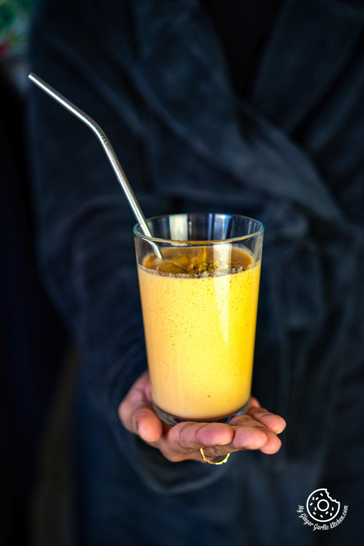 closeup of a hand holding a transparent mango lassi glass with steel straw