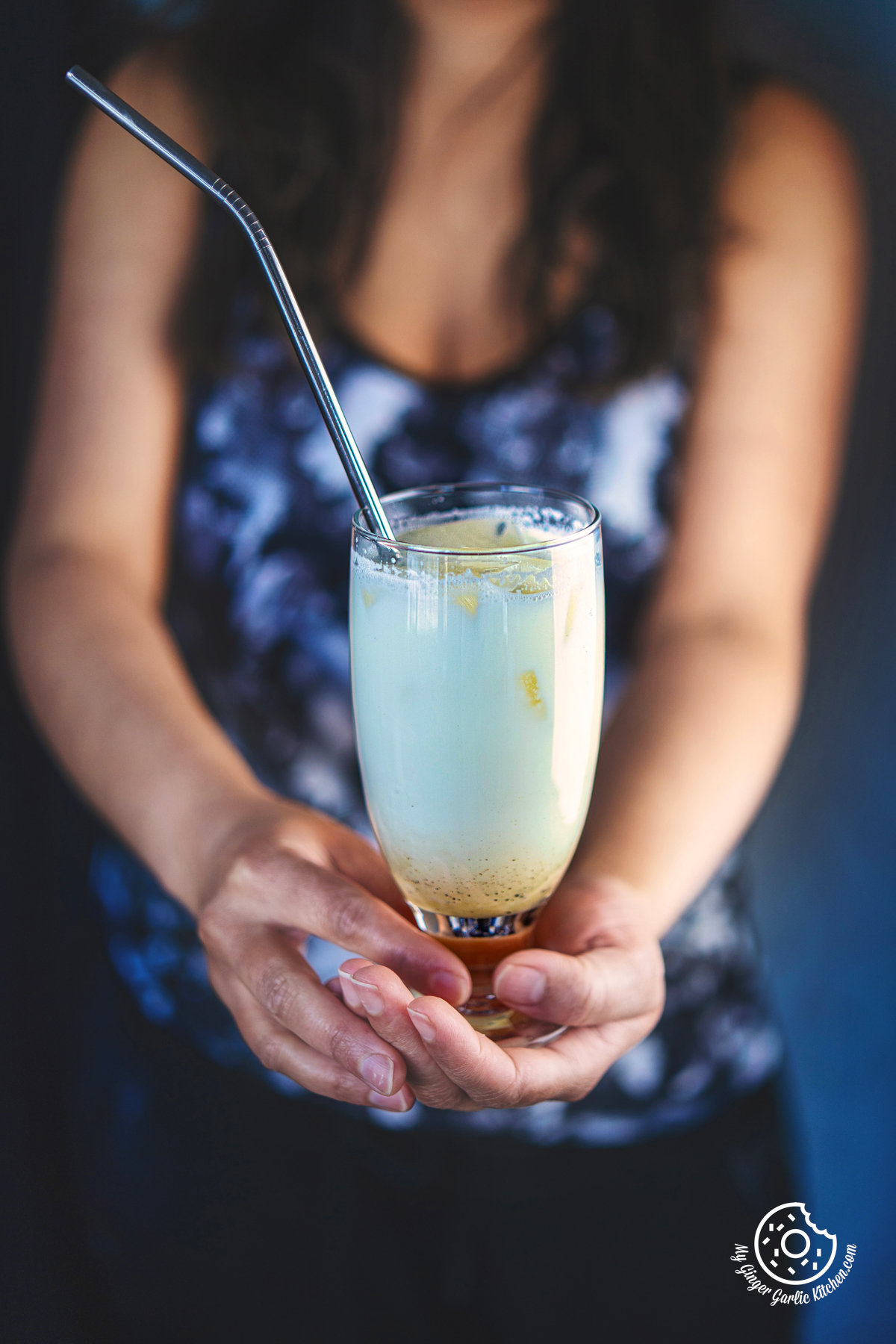 photo of a woman holding a transparent glass of badam sharbat with a metal straw