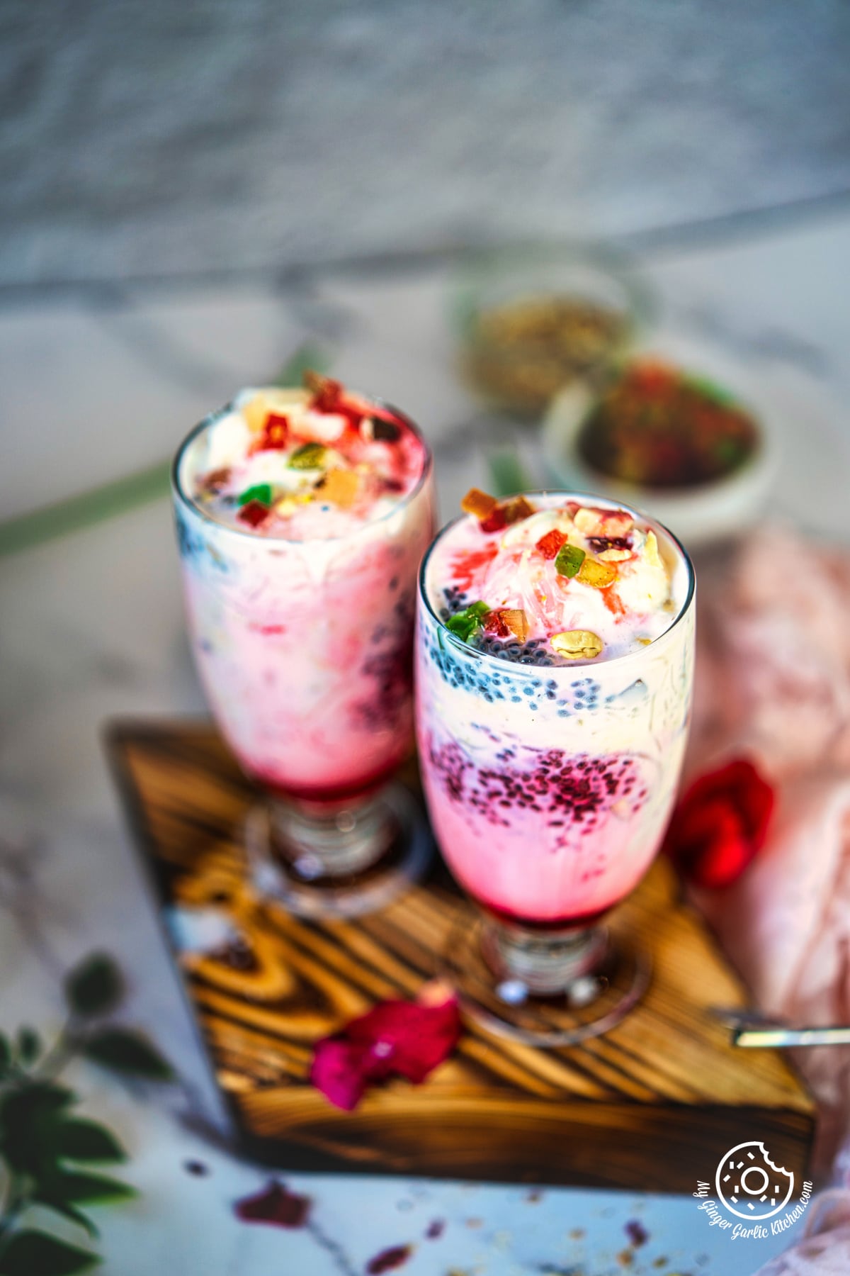 photo of two transparent falooda dessert glasses topped with tutti frutti on a wooden tray