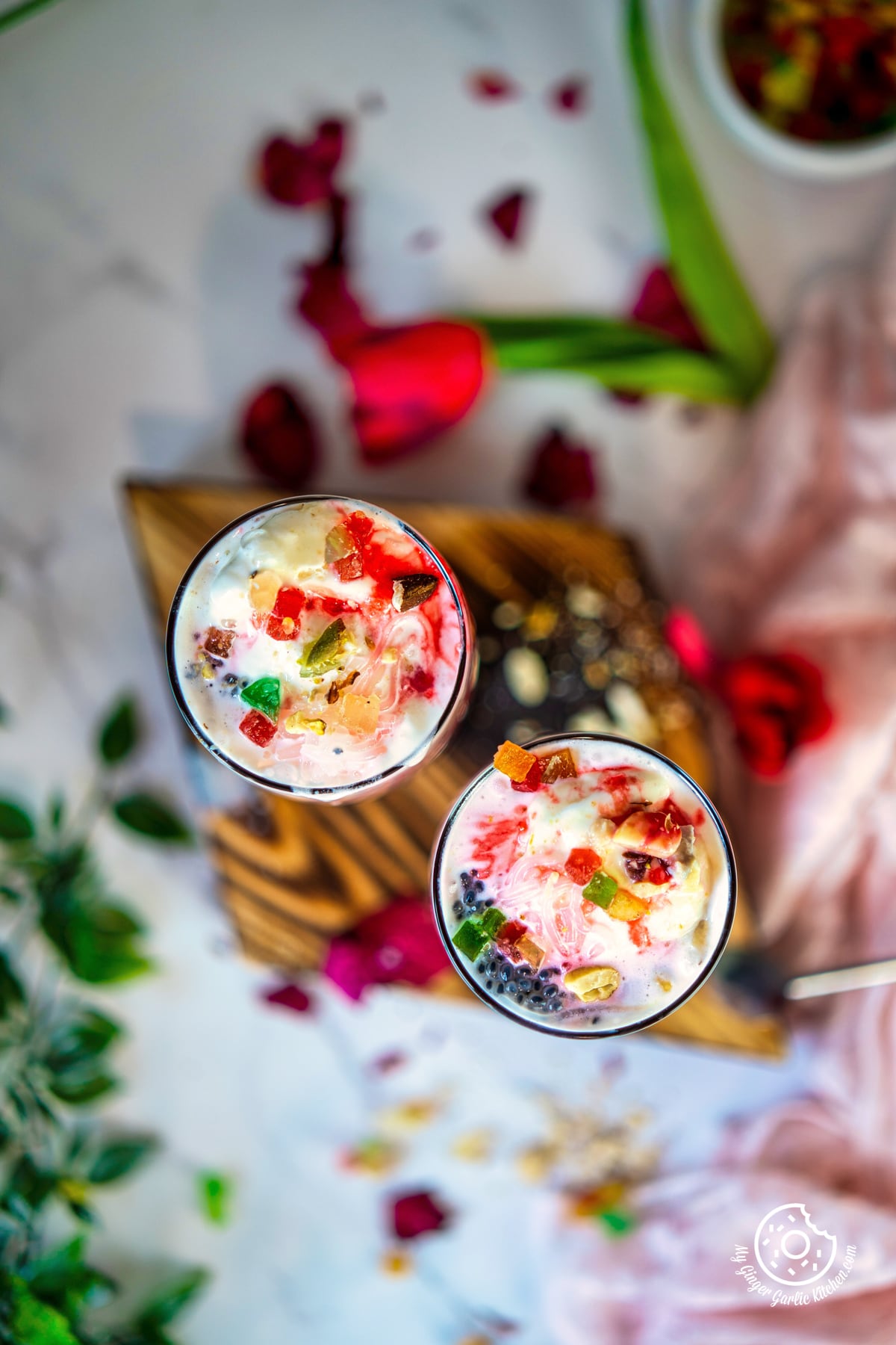 overhead photo of two glasses of falooda with fruit and nuts on a table