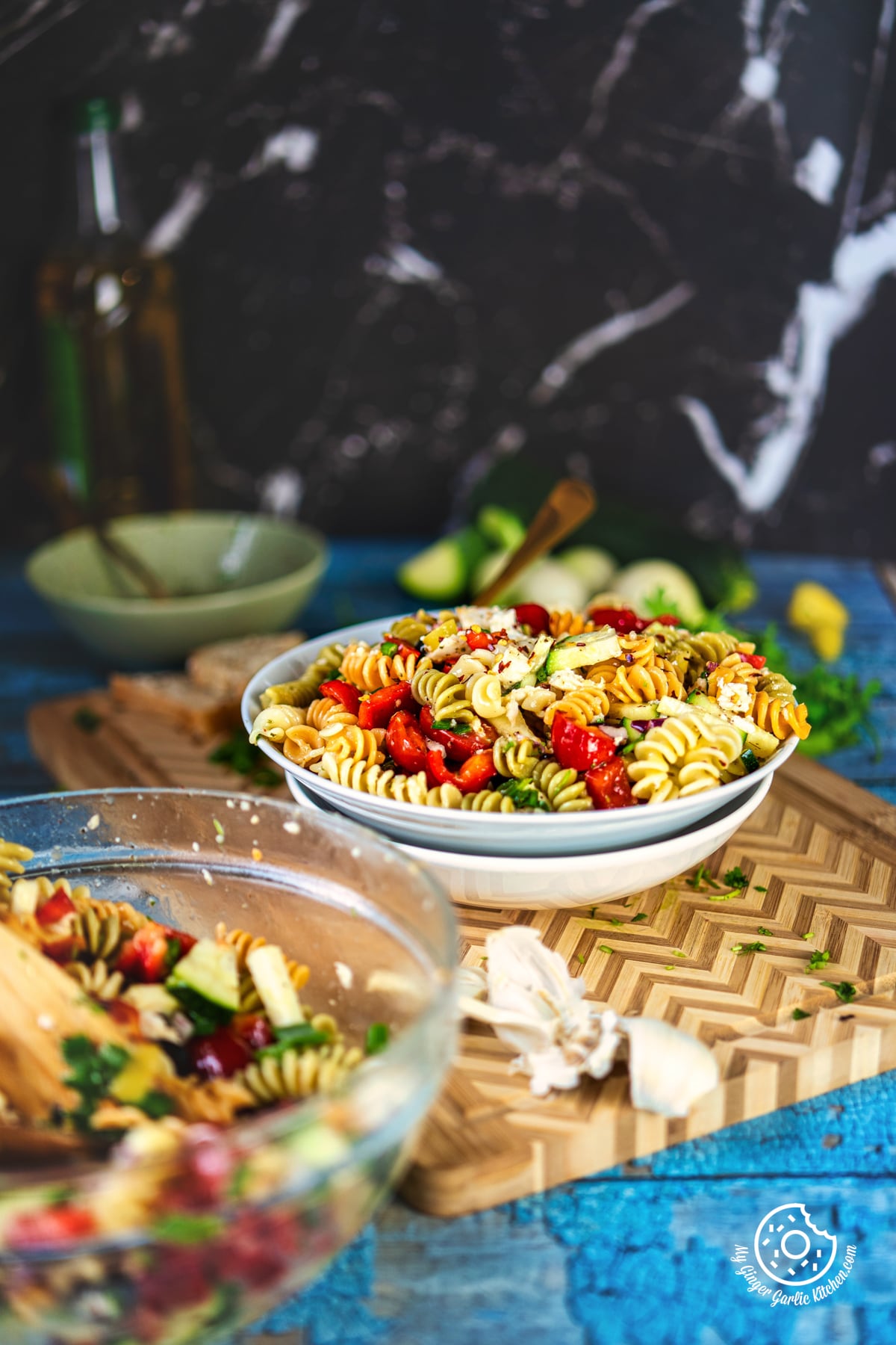 photo of a bowl of pasta salad with a wooden spoon and a bowl of vegetables