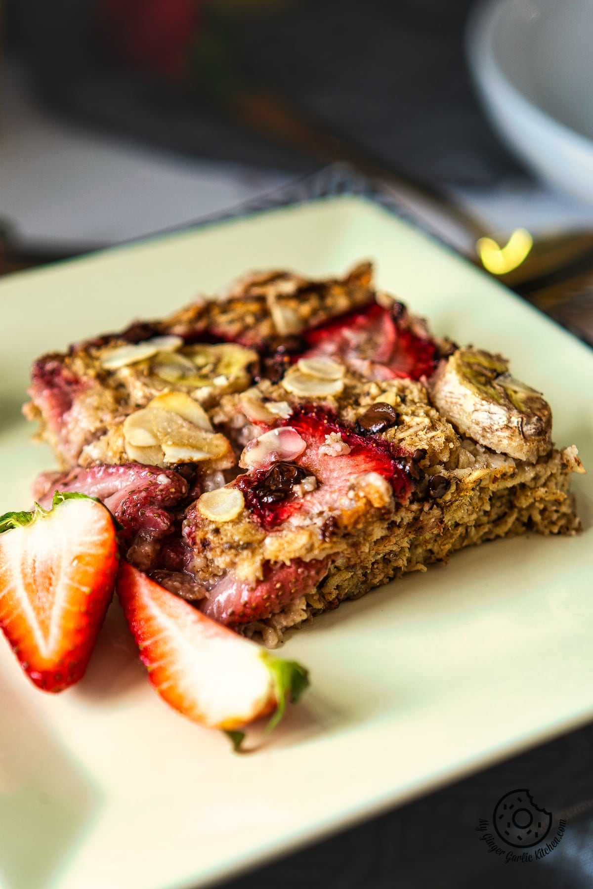 photo of a square plate with a piece of fruit and a piece of strawberry baked oatmeal