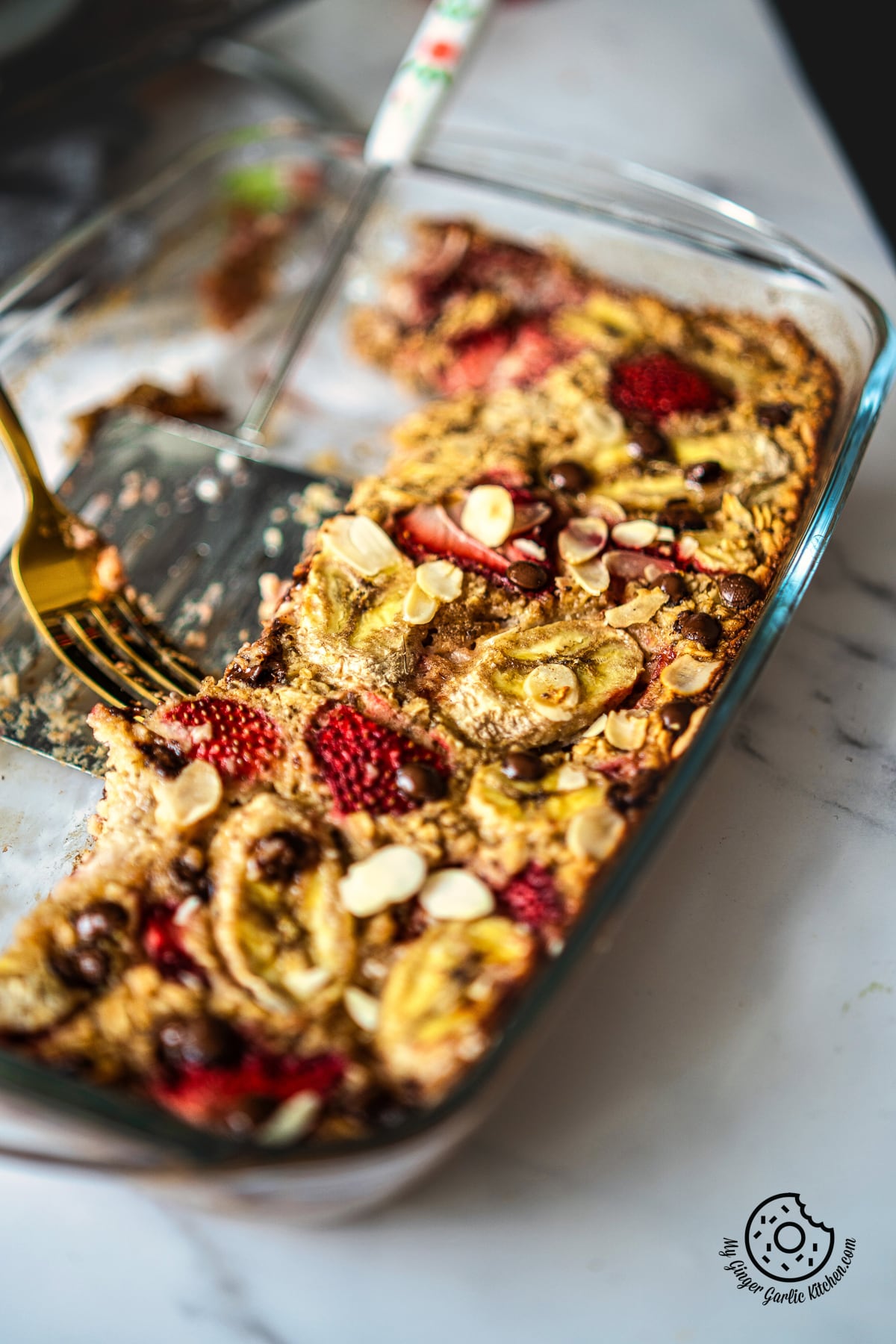 photo of a glass dish with a spoon and 3 pieces od strawberry baked oatmeal