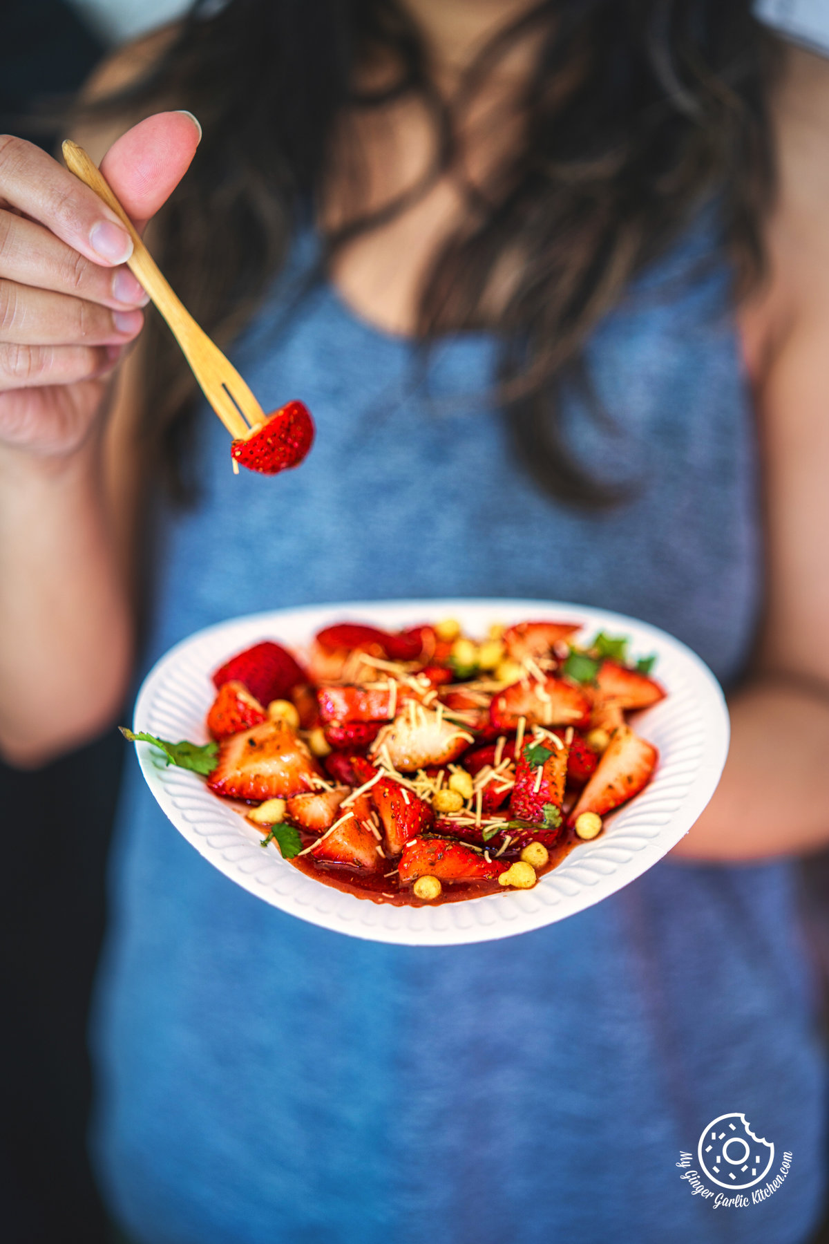 photo of a woman holding a plate of strawberry chaat with a fork