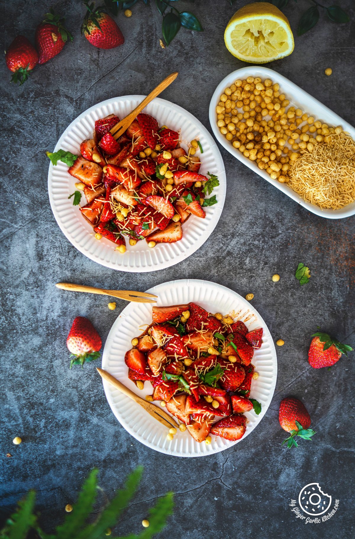 overhead photo of two plates of strawberry chaat on a table with strawberries and lemon