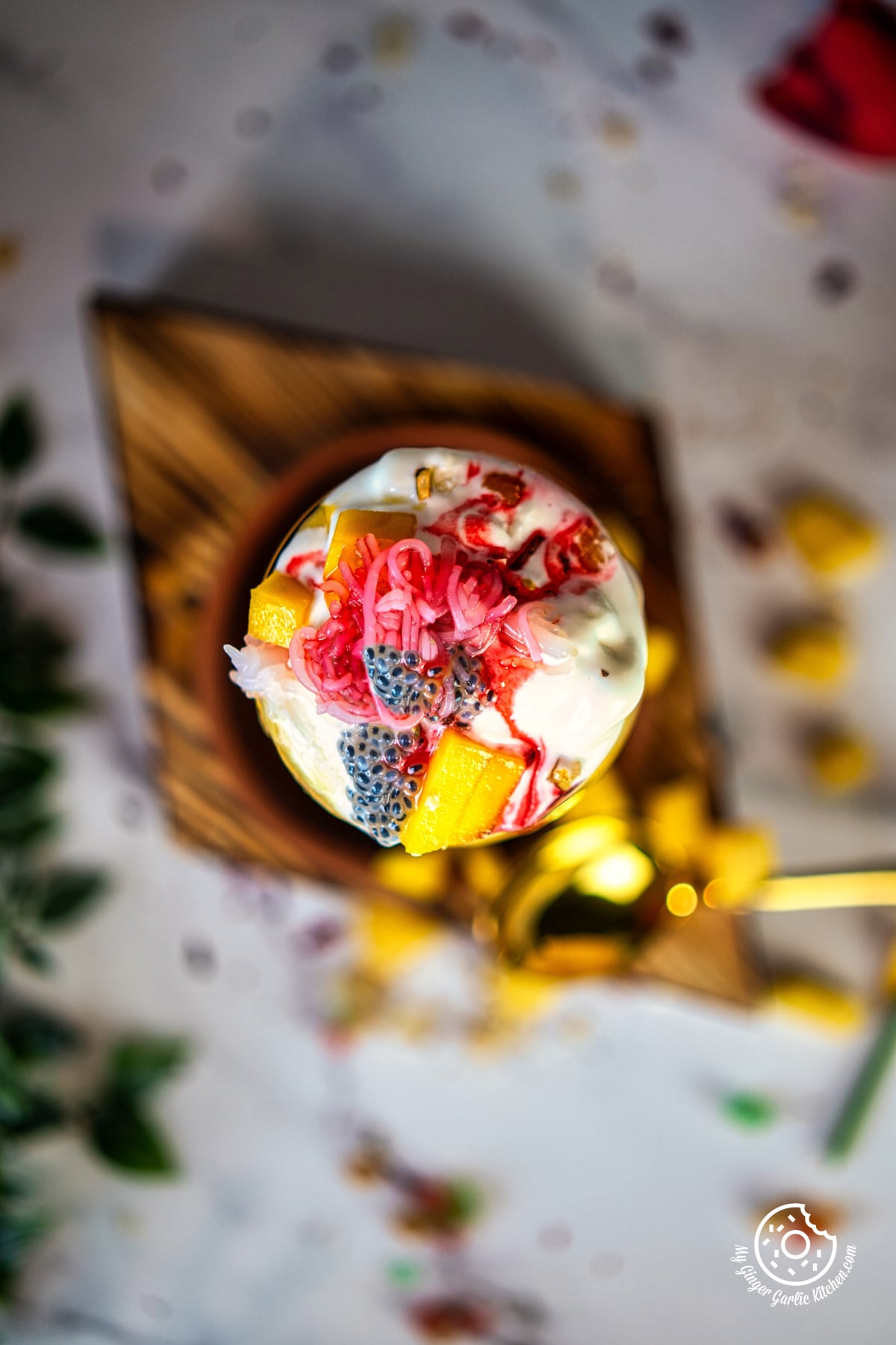 overhead photo of a mango falooda dessert with fruit and cream on a wooden board