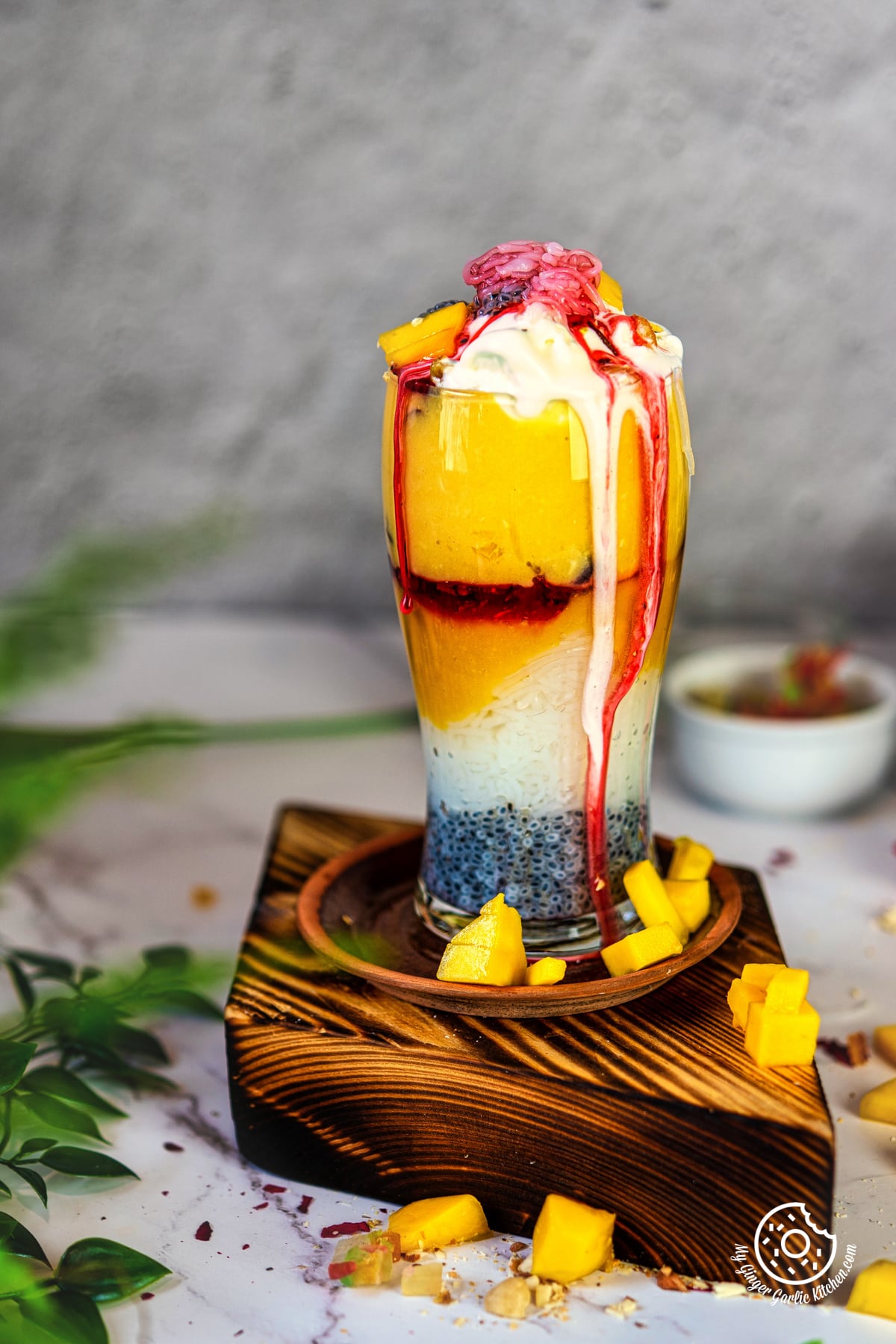 photo of a mango falooda dessert garnished with fruits and ice cream on a wooden tray