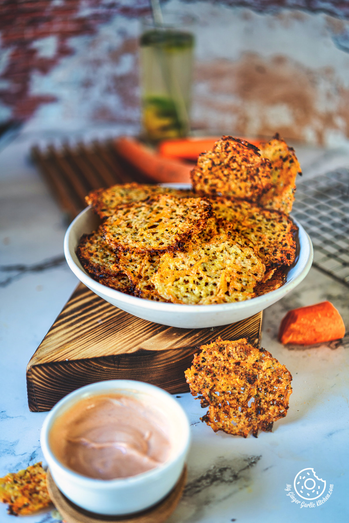 there is a bowl of baked carrot cheese chips on a cutting board with carrots