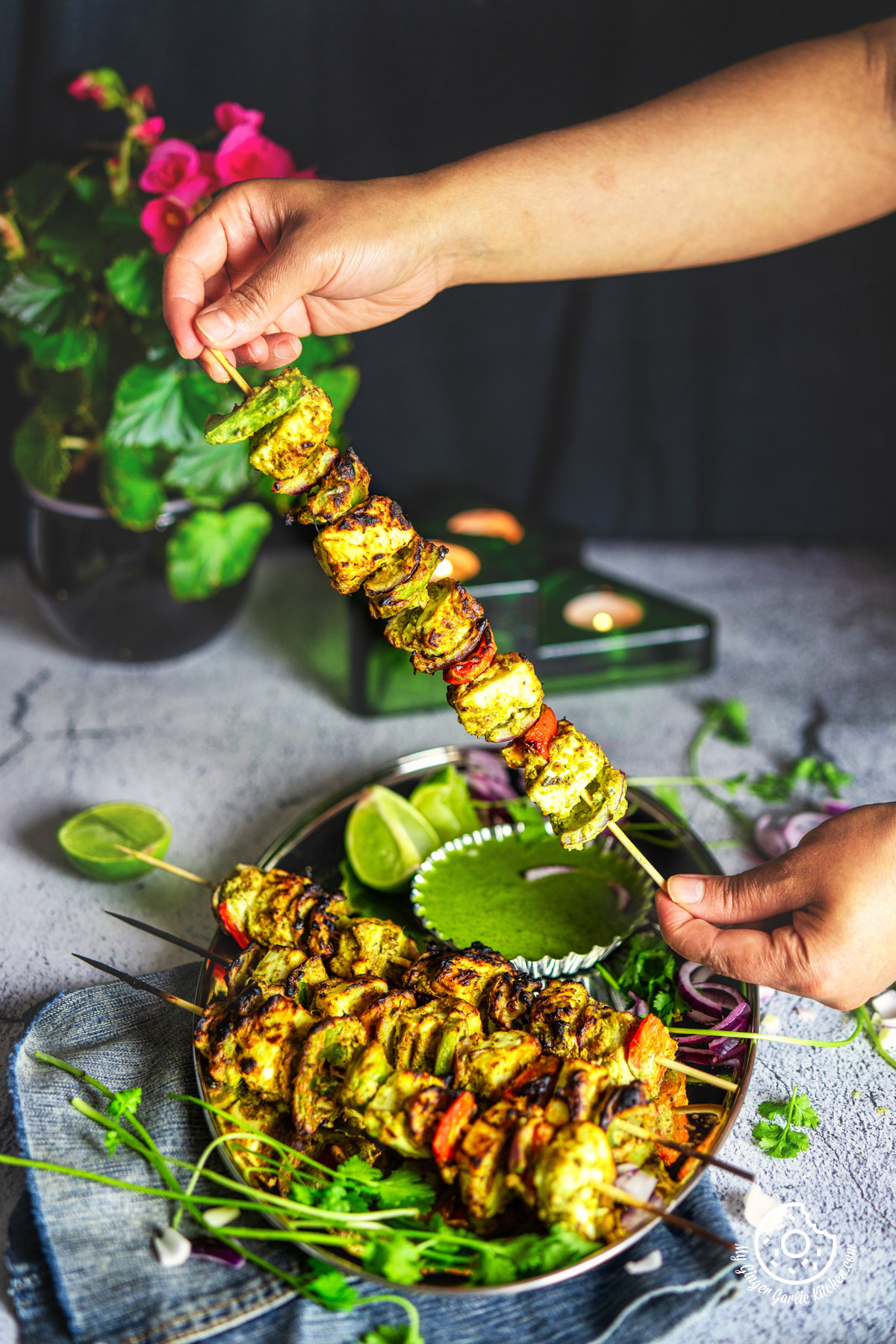 photo of a person is holding a skewer of hariyali paneer tikka on a plate