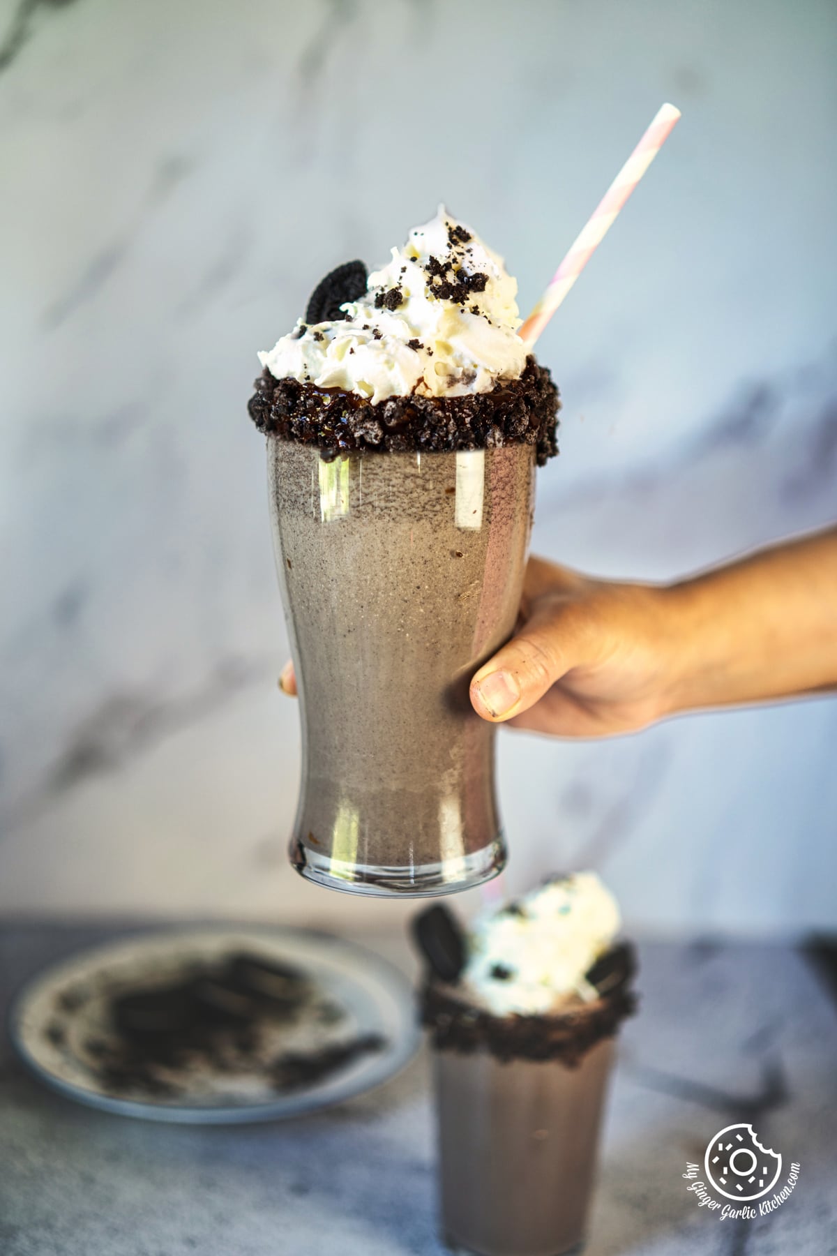 photos of someone holding a tall glass with a chocolate oreo milkshake in it