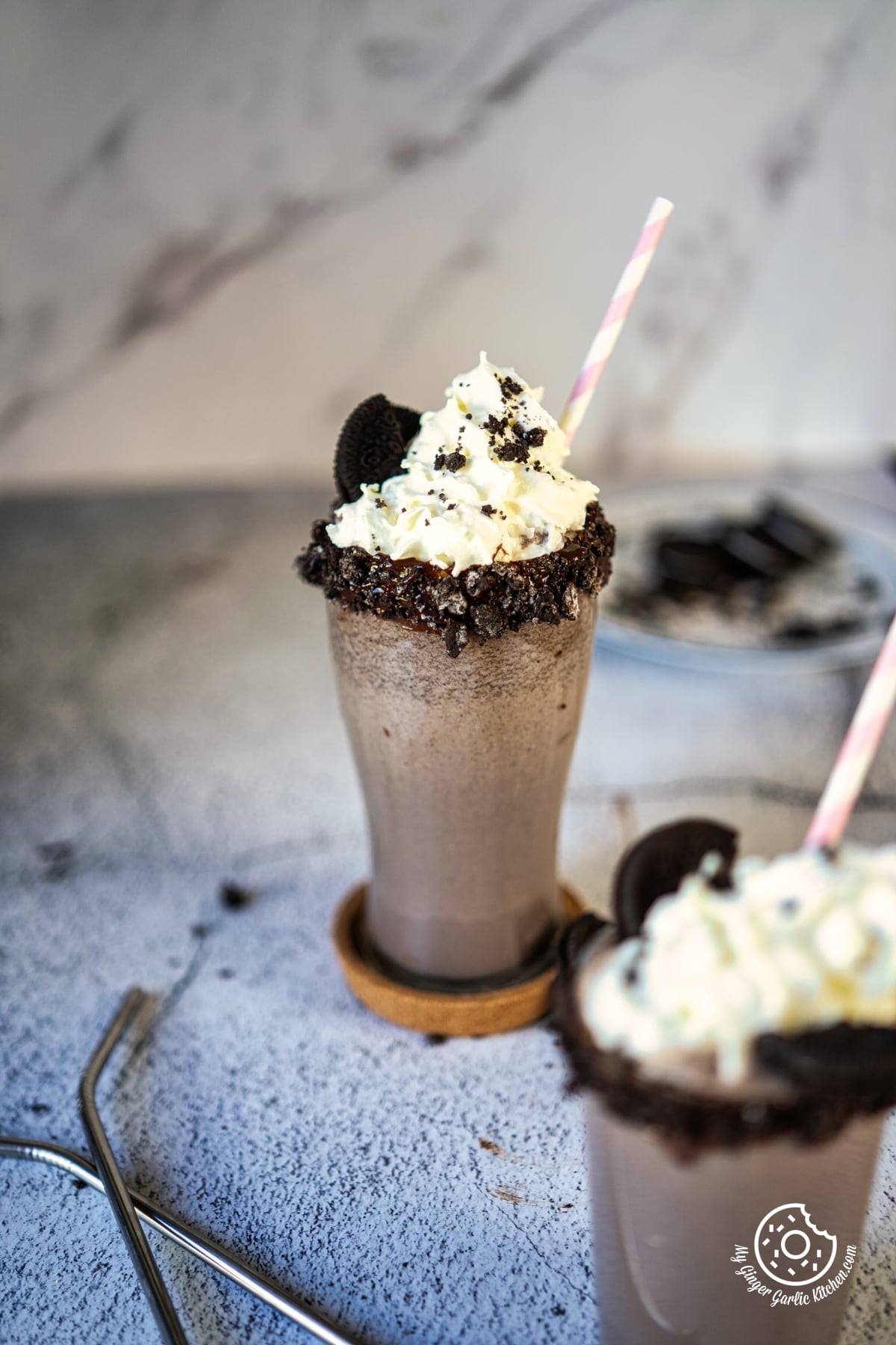 photo of two cups of oreo cookies and oreo milkshake with straws on a table