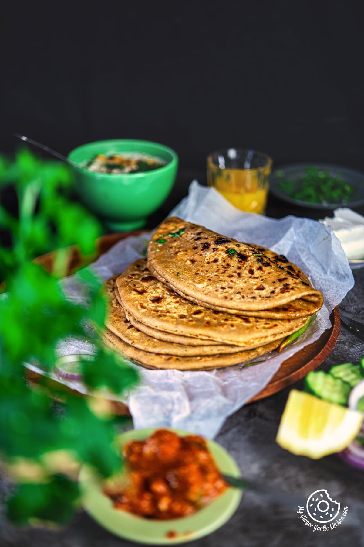 photo of a table with a stack of paneer paratha with pickle on the side