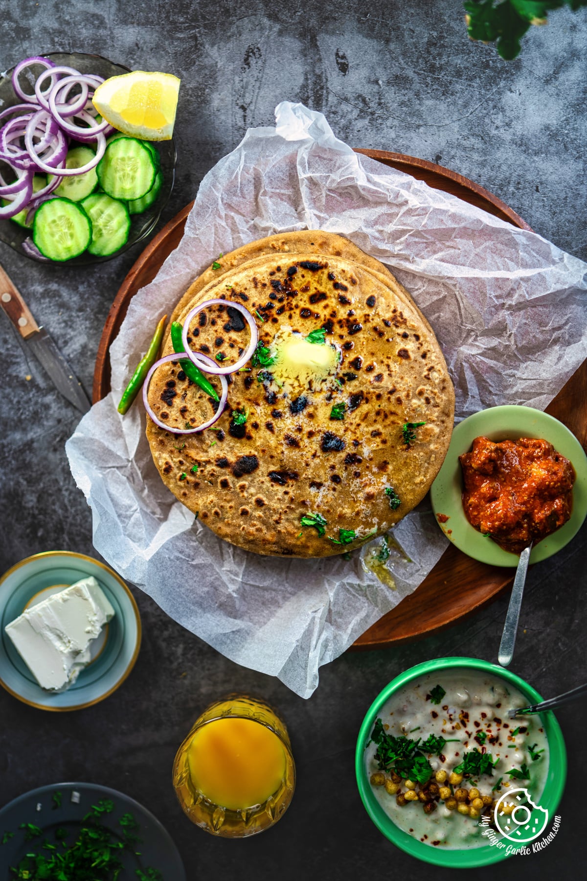 overhead photo of a plate of paneer paratha flat breads with salad, raita and pickle on the side