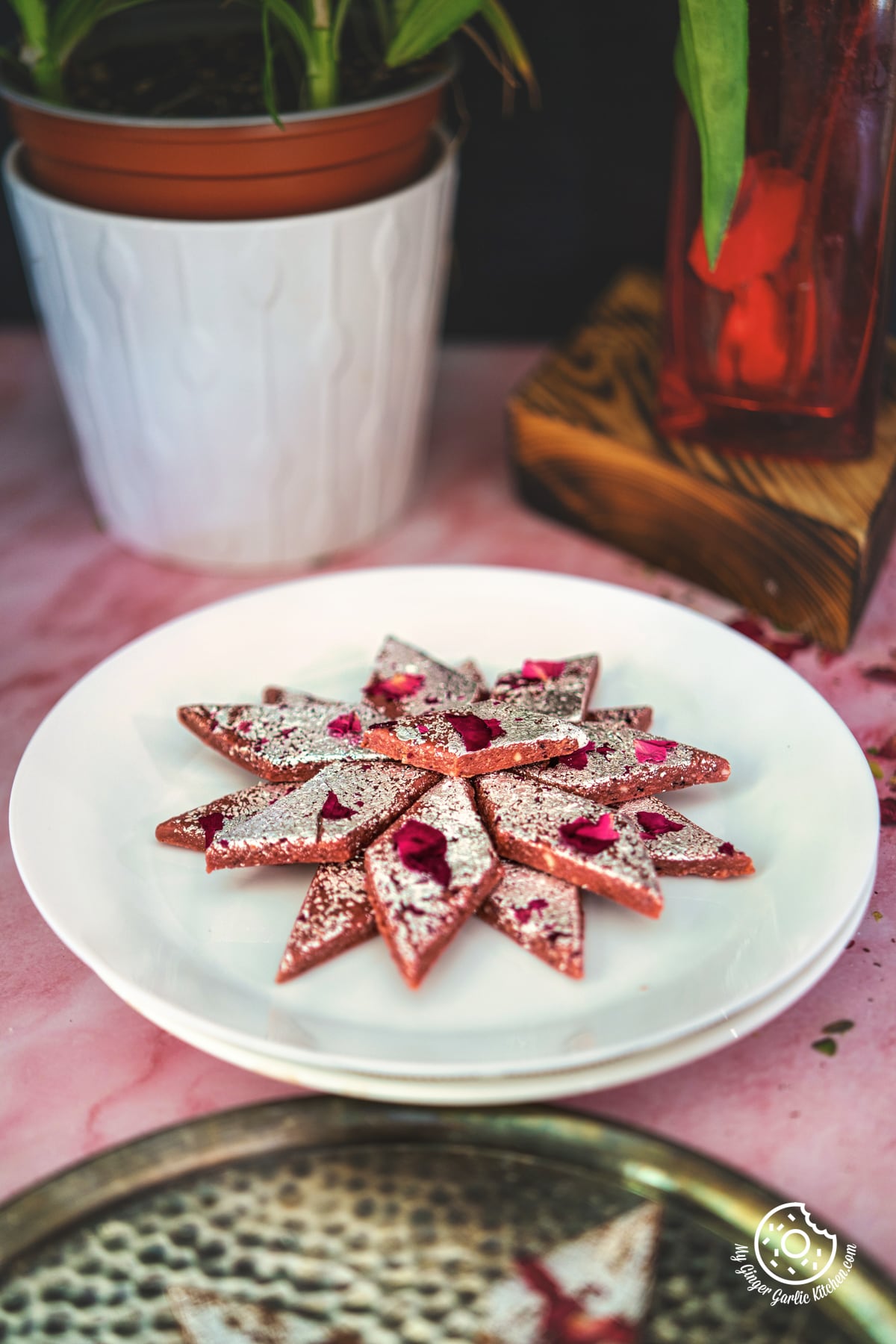 photo of a plate of rose kaju katli on a table with a potted plant