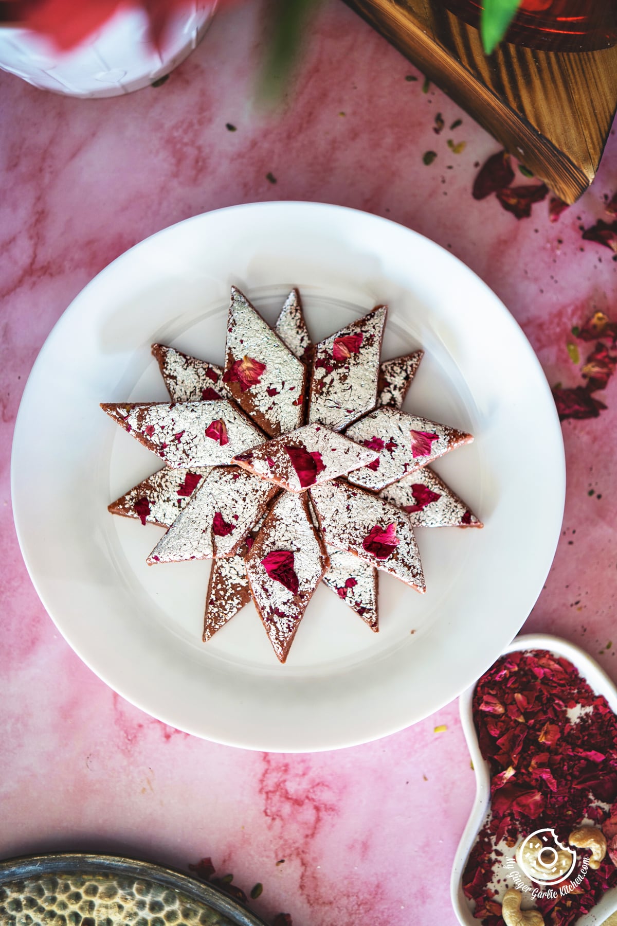 overhead photo of a plate of rose kaju katli dessert on a table with a pink background