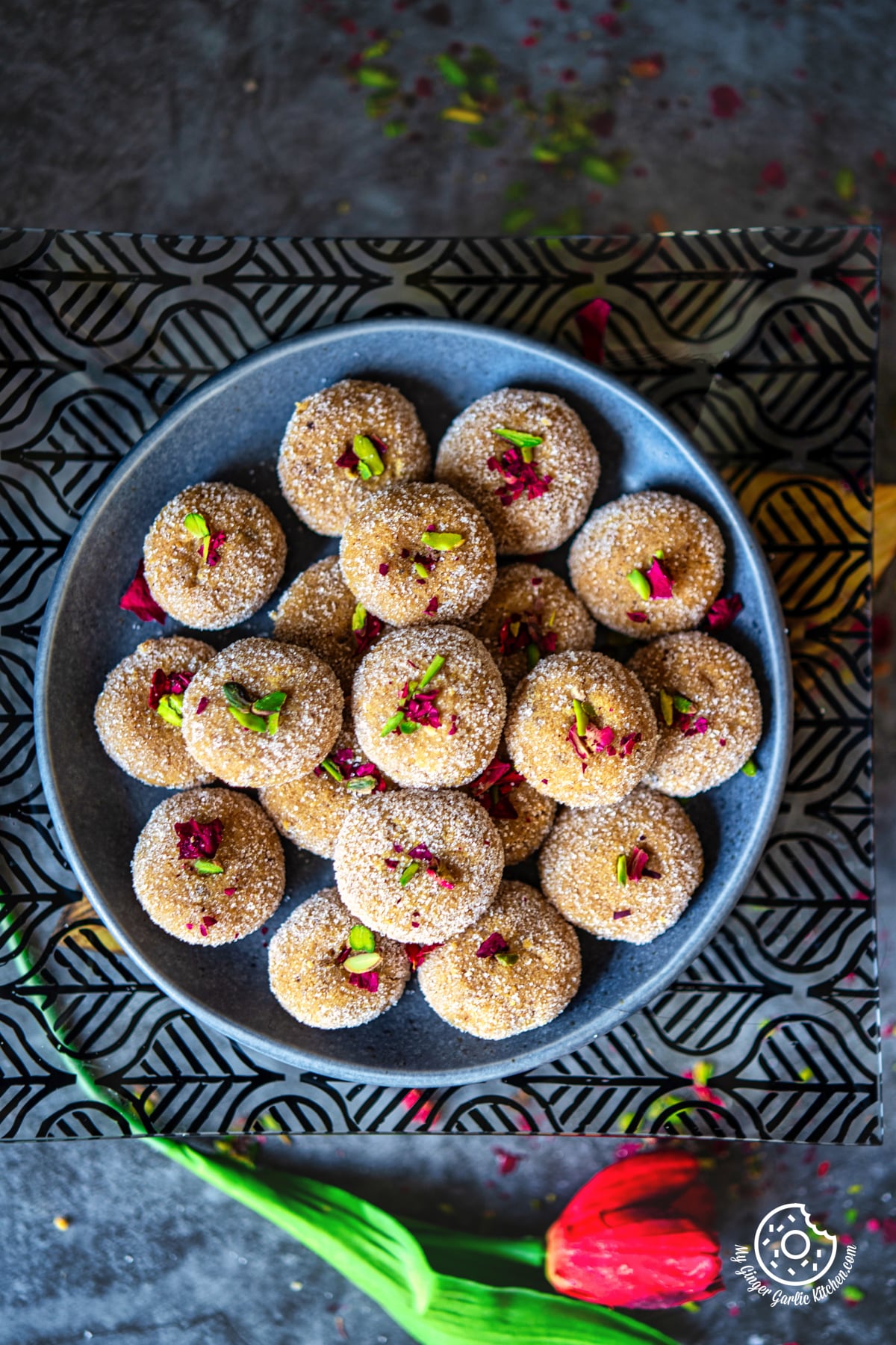 overhead photo of a plate of sugar coated mathura peda with sprinkles and dried rose petals